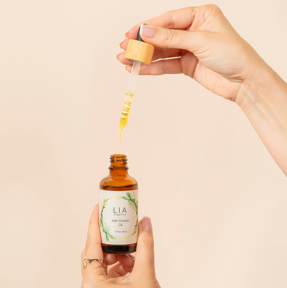 Hands holding Lia Organics Hair Oil and its dropper